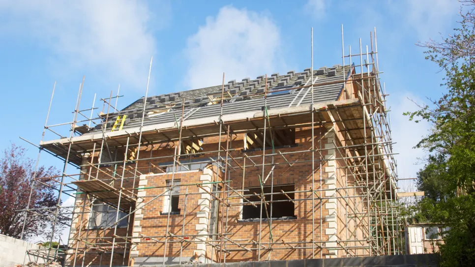 Construcție nouă din cărămidă în faza de acoperire a acoperișului, înconjurată de schele de construcție.